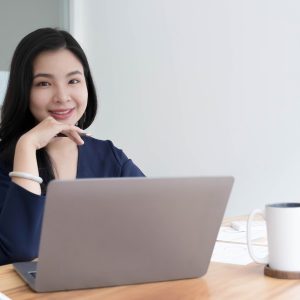 Charming Asian woman working at the office using a laptop Looking at the camera.