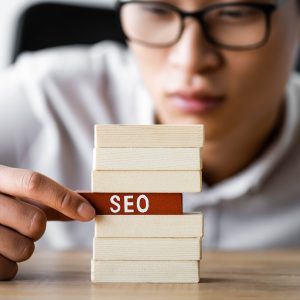 selective focus of asian seo manager holding wooden rectangle with lettering seo