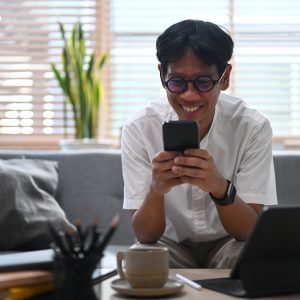 Smiling asian man checking social networking with smart phone at home.